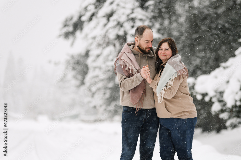 Walk in winter. Embracing couple enjoying snowfall. Man and woman having fun in the frosty forest. Romantic date in winter time.Christmas mood of a young family. Love and leisure concept