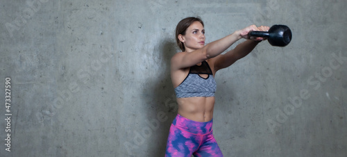 Young athletic woman practicing kettlebell swing against a gray wall. Healthy lifestyle. Strong body © splitov27