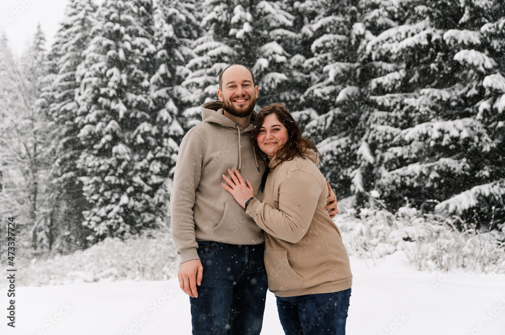 Walk in winter. Embracing couple enjoying snowfall. Man and woman having fun in the frosty forest. Romantic date in winter time.Christmas mood of a young family. Love and leisure concept Walk in winter. Embracing couple enjoying snowfall. Man and woman having fun in the frosty forest. Romantic date in winter time.Christmas mood of a young family. Love and leisure concept