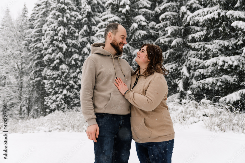 Walk in winter. Embracing couple enjoying snowfall. Man and woman having fun in the frosty forest. Romantic date in winter time.Christmas mood of a young family. Love and leisure concept Walk in winter. Embracing couple enjoying snowfall. Man and woman having fun in the frosty forest. Romantic date in winter time.Christmas mood of a young family. Love and leisure concept