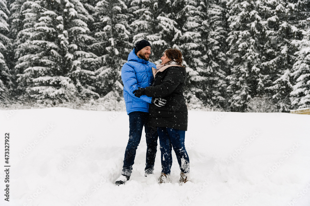 Walk in winter. Embracing couple enjoying snowfall. Man and woman having fun in the frosty forest. Romantic date in winter time.Christmas mood of a young family.  Love and leisure concept