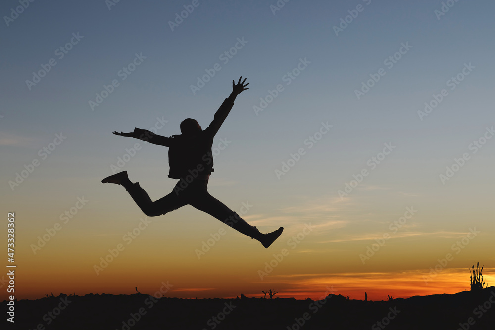 Silhouette of happy girl jumping playing on mountain at sunset or sunrise