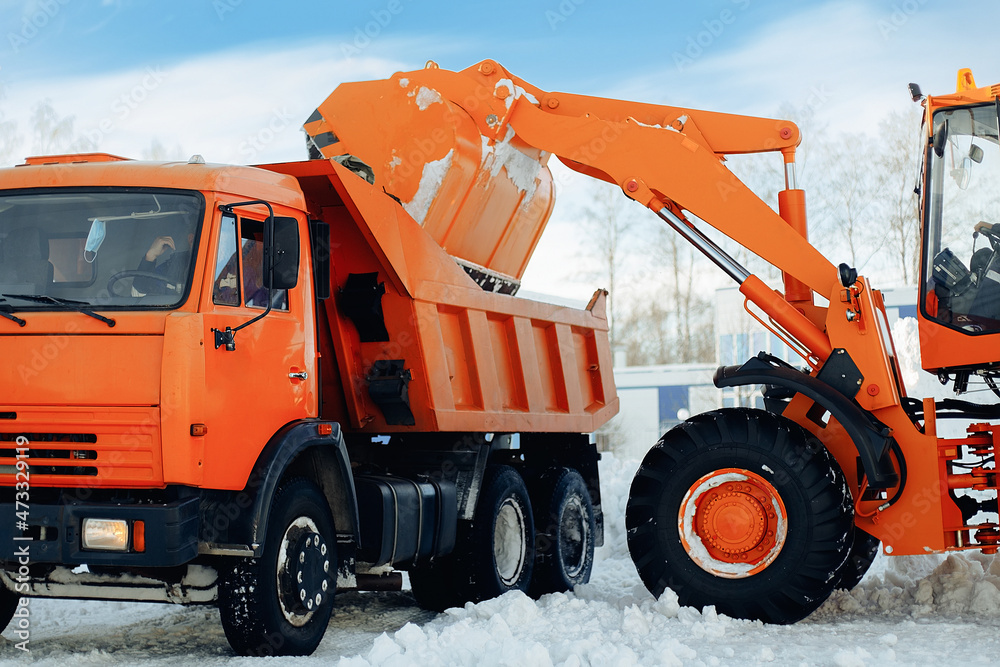 Removal of snow from streets after snowfall. Tractor loads bucket of snow into truck. Work of utilities in winter. Industrial background. Real scene of work. Removal of snow from streets after snowfall. Tractor loads bucket of snow into truck. Work of utilities in winter. Industrial background. Real scene of work.