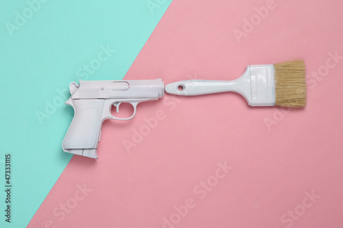 White gun with paint brush on blue pink background. Minimal, creative layout, top view photo