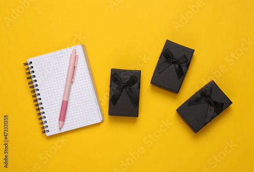 Notebook with black gift boxes on yellow background. Top view