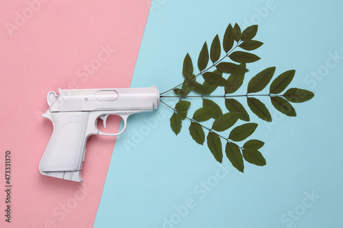 White gun with green leaves on blue pink background. Minimal, creative layout, say no war photo