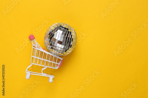 Shopping cart with disco ball on yellow background. Party concept. Creative minimal layout. Top view