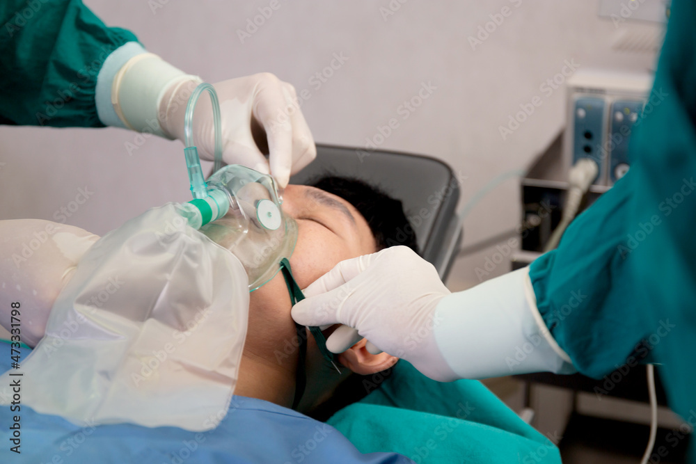 Closeup hands of doctor and assistant holding oxygen mask with patient emergency in the operation room at hospital, surgeon healing and surgery, problem of breathing, instruments medical and health.