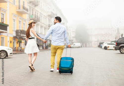 International loving couple of tourists with travel luggage strolling along a foggy European street
