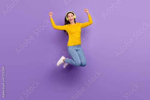 Full length photo of young girl have fun jump rejoice victory listen radio earphones isolated over purple color background