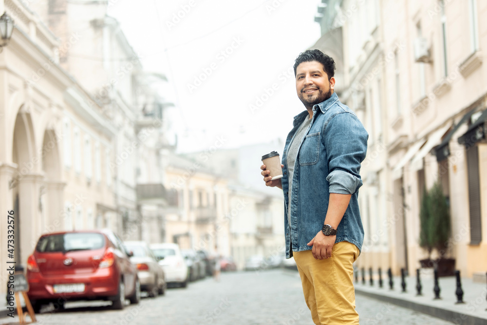 Handsome smiling hispanic guy drinking coffee in the city