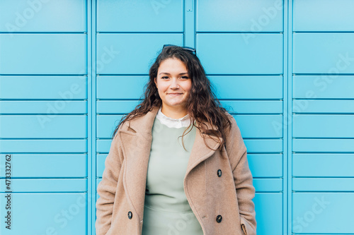 Smiling curvy woman wearing overcoat in front of blue wall photo