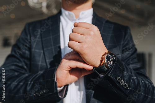 A stylish man, a businessman in a plaid blue suit, a white shirt with a wristwatch, buttons a button on his hand, getting ready for work.