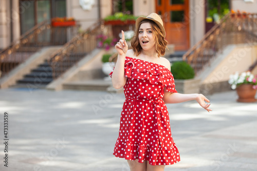 Portrait of shocked beautiful woman in red polka dot dress and hat in city
