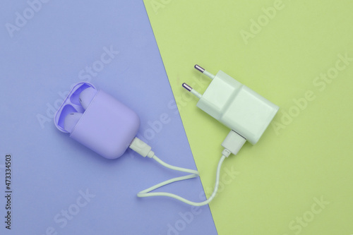 Wireless headphones with charging case and charging adapter on a blue-pink pastel background. Top view