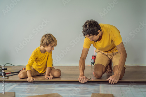 Father and son installing new wooden laminate flooring on a warm film floor. Infrared floor heating system under laminate floor photo