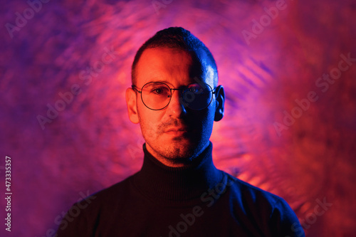 Neon portrait of serious man wearing glasses with black frame and dark turtleneck sweater on cosmic silver multicolored background