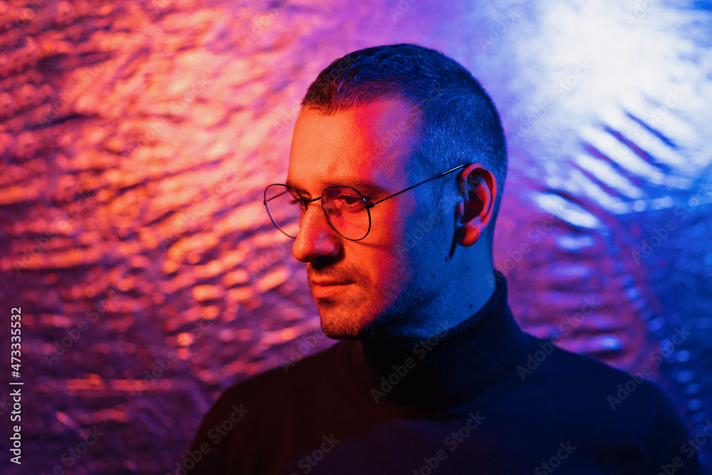 Neon portrait of serious man wearing glasses with black frame and dark turtleneck sweater on cosmic silver multicolored background Neon portrait of serious man wearing glasses with black frame and dark turtleneck sweater on cosmic silver multicolored background