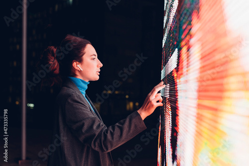 Businesswoman with earphones using touch screen interactive information booth at night photo