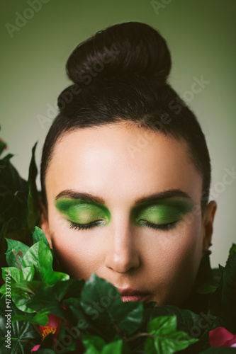 Woman with eye make-up and green plants against green background