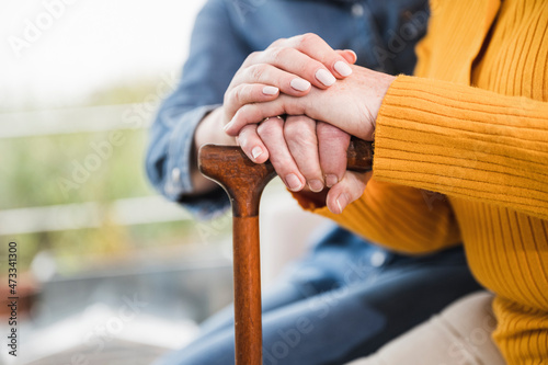 Caregiver and woman's hands stacked on walking cane photo