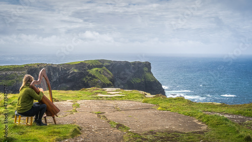Fényképezés Woman playing harp on the top of iconic Cliffs of Moher, popular tourist attract