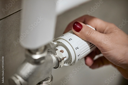 Woman adjusting thermostatic radiator valve of heating boiler at home photo