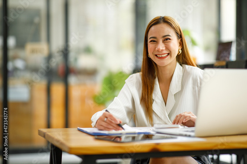 Confident businesswoman documents working on laptop at her workplace at modern office. reading financial report analyzing statistics pointing at pie chart working at her desk.