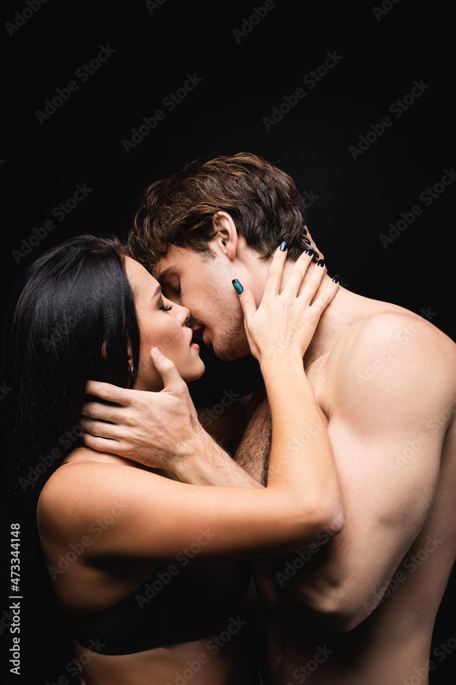 side view of young couple with closed eyes hugging while kissing isolated on black.