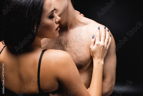 brunette woman in underwear hugging shirtless boyfriend on black.