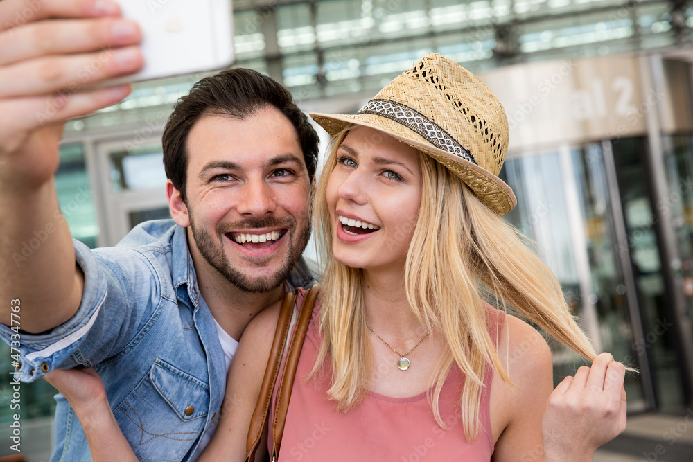 Young couple taking selfie through smart phone outside airport terminal Young couple taking selfie through smart phone outside airport terminal
