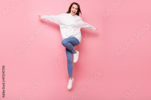 Photo of sweet adorable young lady wear white hoodie smiling jumping high hands sides isolated pink color background