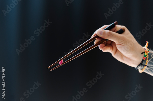Man holding capsule with chopsticks against black background photo