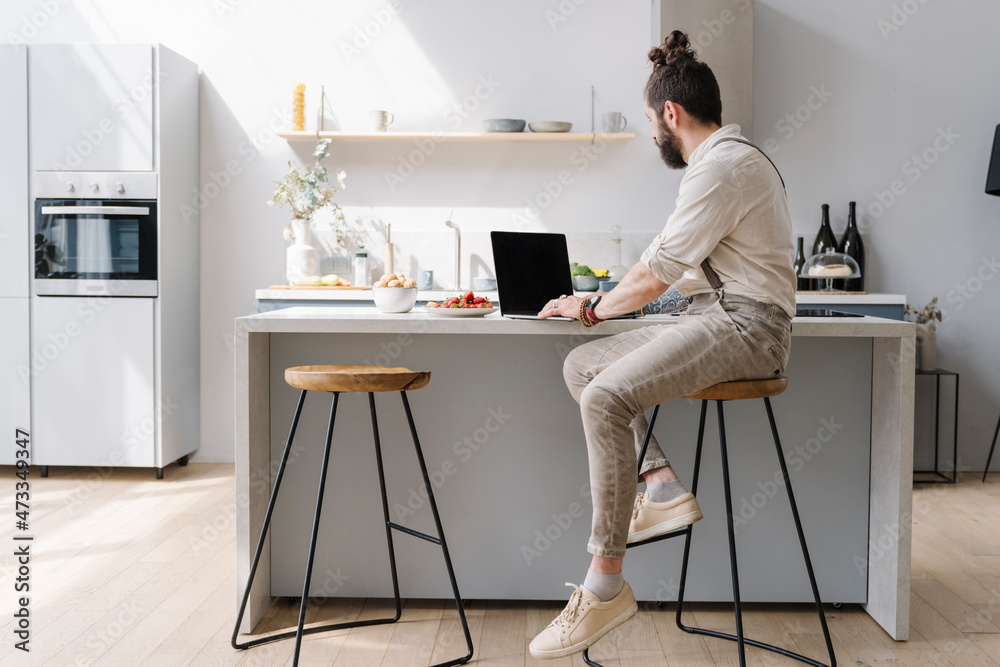 Mid adult man using laptop while sitting in kitchen at home Mid adult man using laptop while sitting in kitchen at home