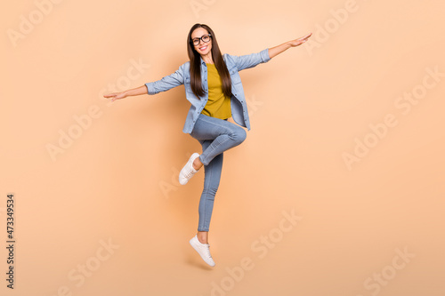 Full size photo of positive beautiful funky lady jumping spread hands plane pose isolated on beige color background