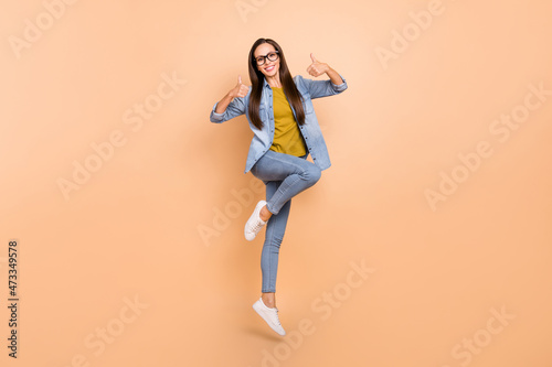 Full size photo of pretty female jumping show thumb-up recommending wear denim clothes isolated on beige color background