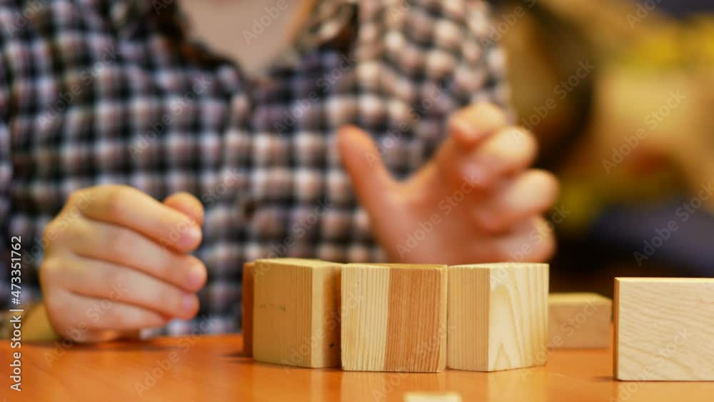 Caucasian boy of 6-7 years old with concentration plays with cubes and builds a tower. The child spends his leisure time playing a board game. Develop creativity in children. selective focus