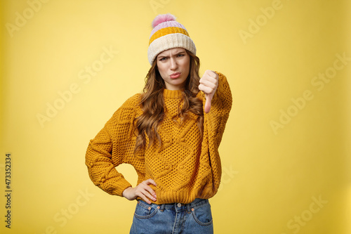 Lame dislike unfollow. Portrait disappointed displeased picky young judgemental woman show thumb-down cringing grimacing unsatisfied expressing disapproval antipathy, yellow background photo
