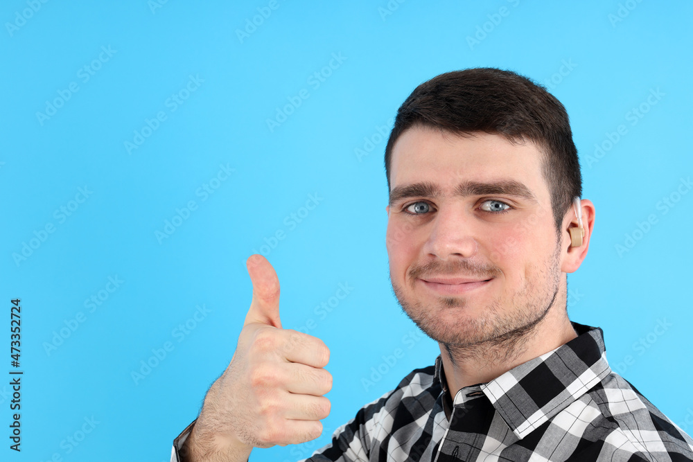 Young man with hearing aid on blue background Young man with hearing aid on blue background