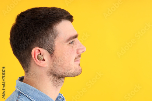 Young man with hearing aid on yellow background