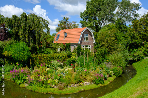 Netherlands, North Holland, Hoorn, Lake Ijssel ditch stretching in front of blooming garden of rustic house photo