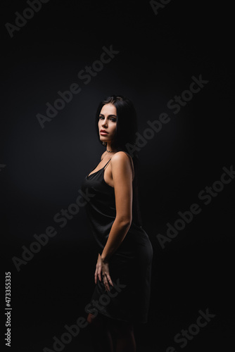 brunette young woman in slip dress standing isolated on black.