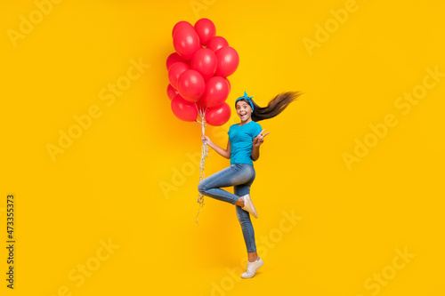 Full size profile side photo of young excited teenager girl show v-symbol many balloons festive isolated over yellow color background