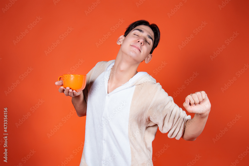Cheerful man in pajamas with a mug of coffee on an orange background. Cheerful man in pajamas with a mug of coffee on an orange background.