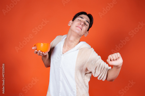 Cheerful man in pajamas with a mug of coffee on an orange background.