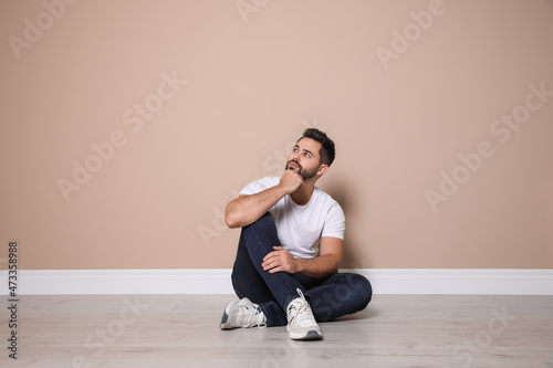 Young man sitting on floor near beige wall indoors