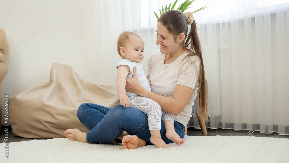 Smiling mother and baby son looking at working robot vacuum cleaner cleaning carpet in living room. Concept of hygiene, household gadgets and robots at modern life.
