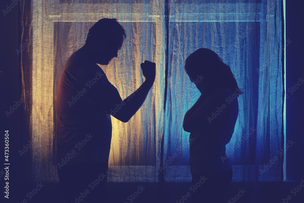 Silhouette of quarreling man and woman at the night window. Married couple husband and wife, violence in evening light of home living room