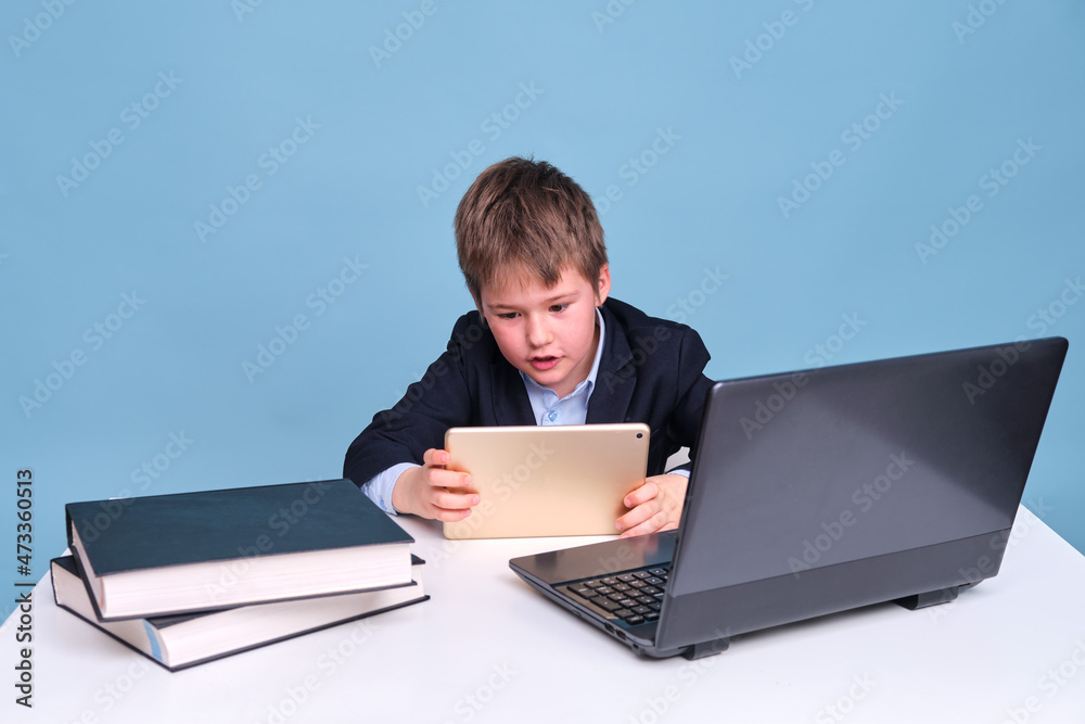 A boy in a school suit with a digital tablet in his hands on distance learning, copy space on a blue studio background