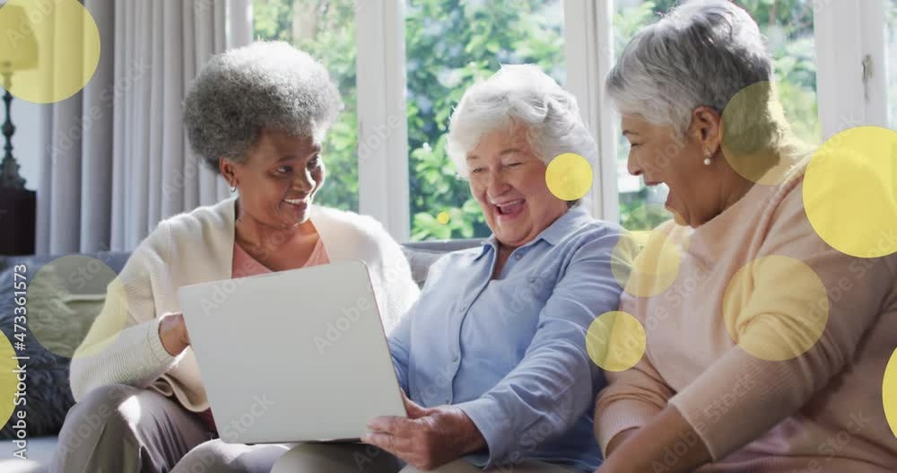 Animation of happy senior diverse female friends using laptop over light spots Animation of happy senior diverse female friends using laptop over light spots